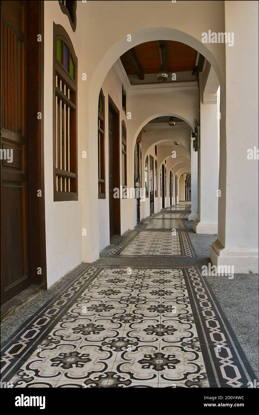 A ground perspective view down a corridor of traditional chinese peranakan shophouses, with arched columns and ornate tiled flooring. Stock Photo