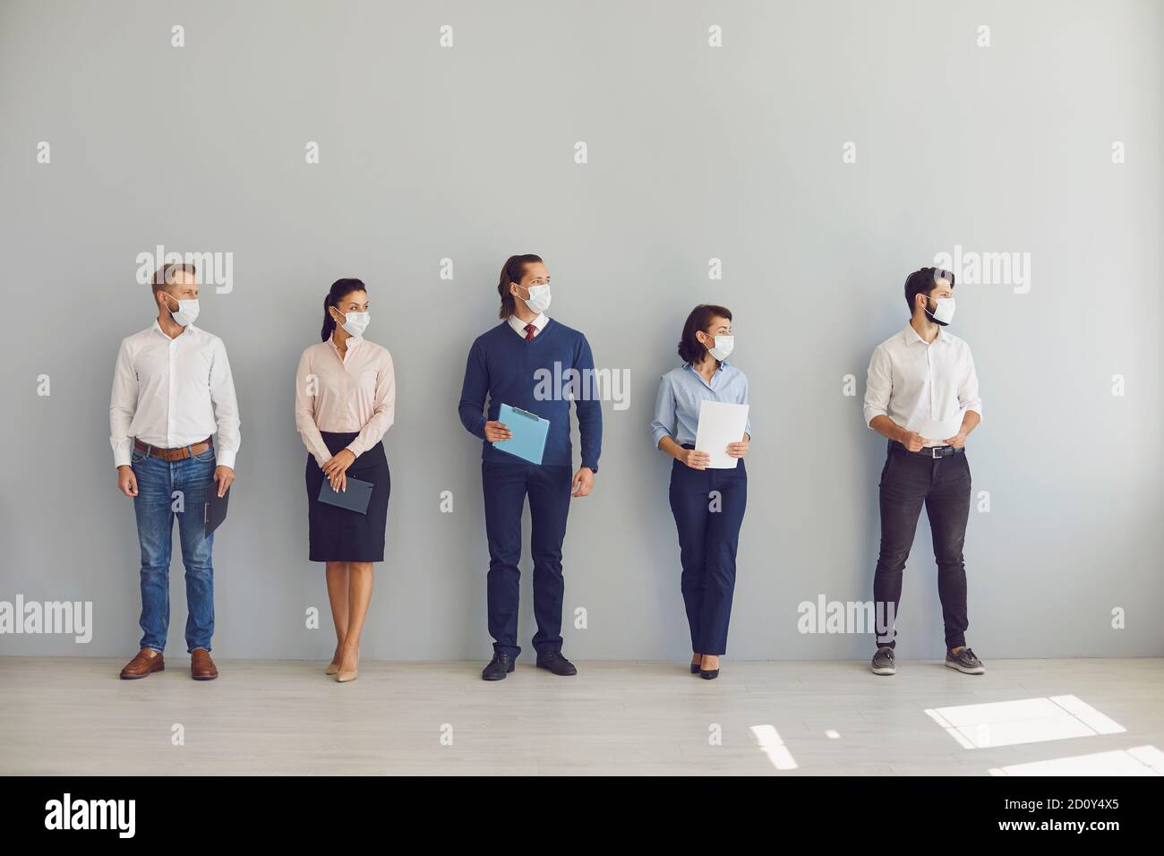 Job seekers in face masks waiting for job interview standing in corridor keeping safe distance Stock Photo