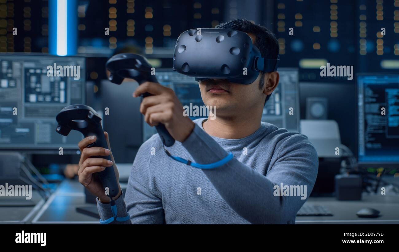 Software Delevoper Wearing Virtual Reality Headset Using Controllers to Develop and Program VR Gaming and Applications. In the Background Technology Stock Photo