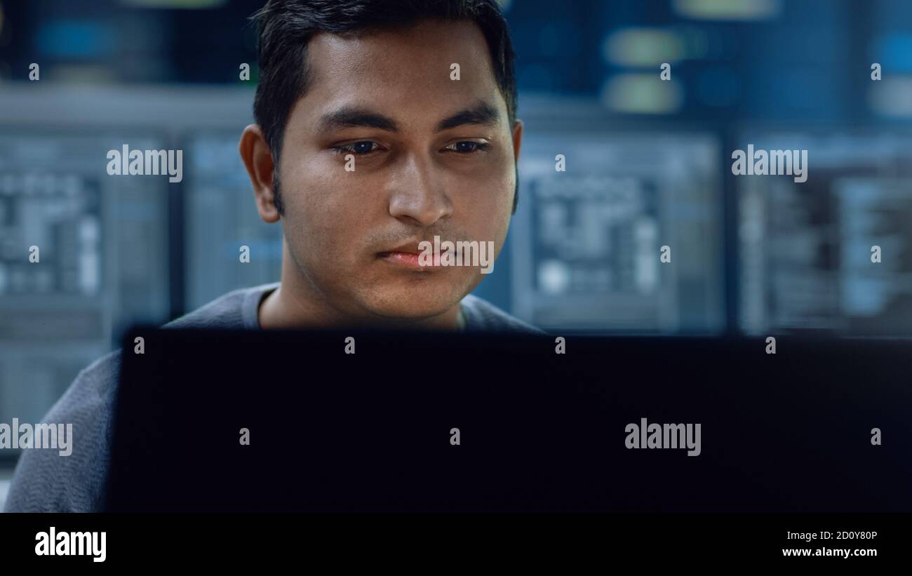 Portrait of a Smart and Handsome IT Specialist Working on a Personal Computer. In the Background Unfocused Personal Computers with Screens in Stock Photo