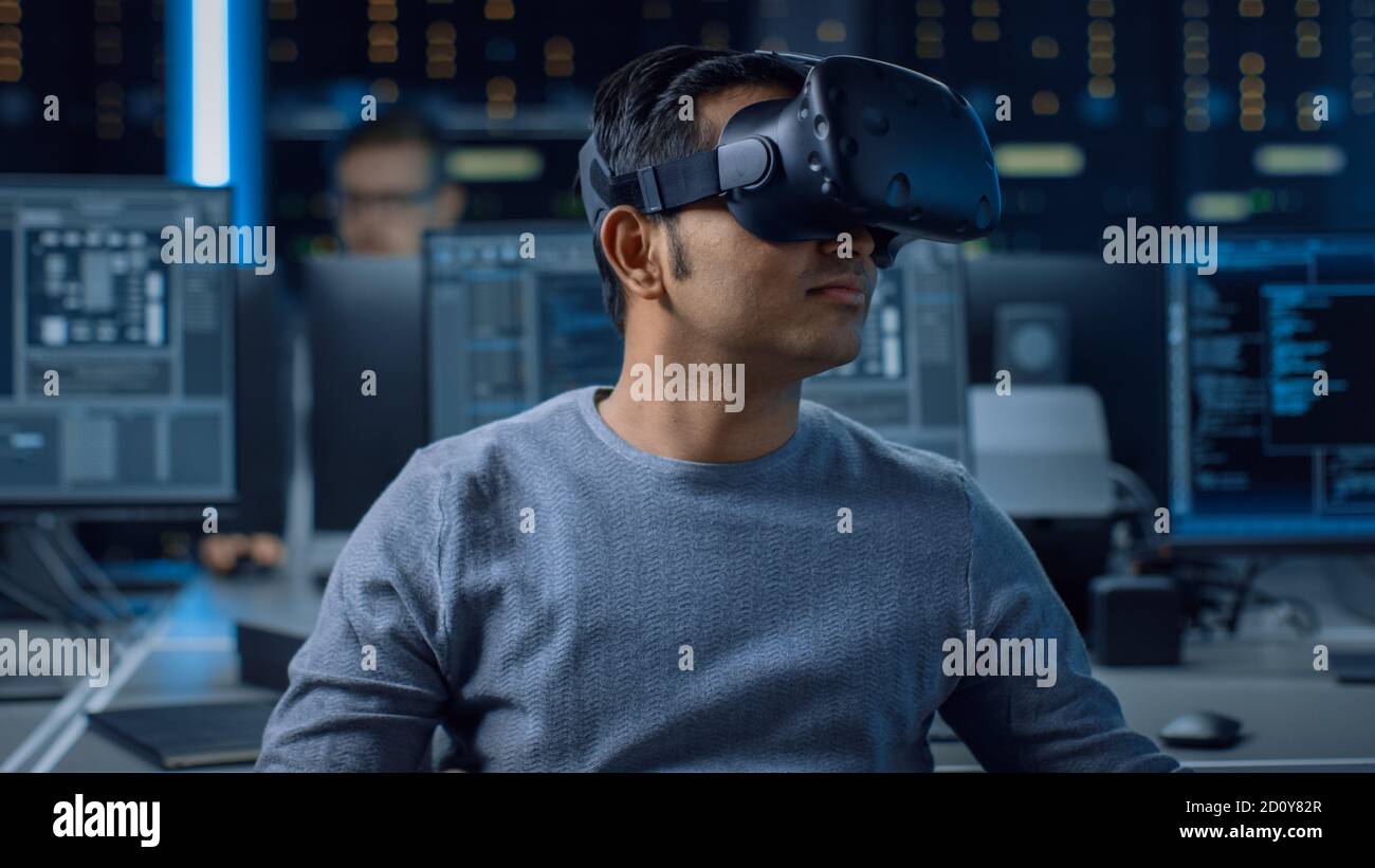 Software Delevoper Wearing Virtual Reality Headset on His Head, Developing and Programming VR Game or Application. In the Background Technology Stock Photo