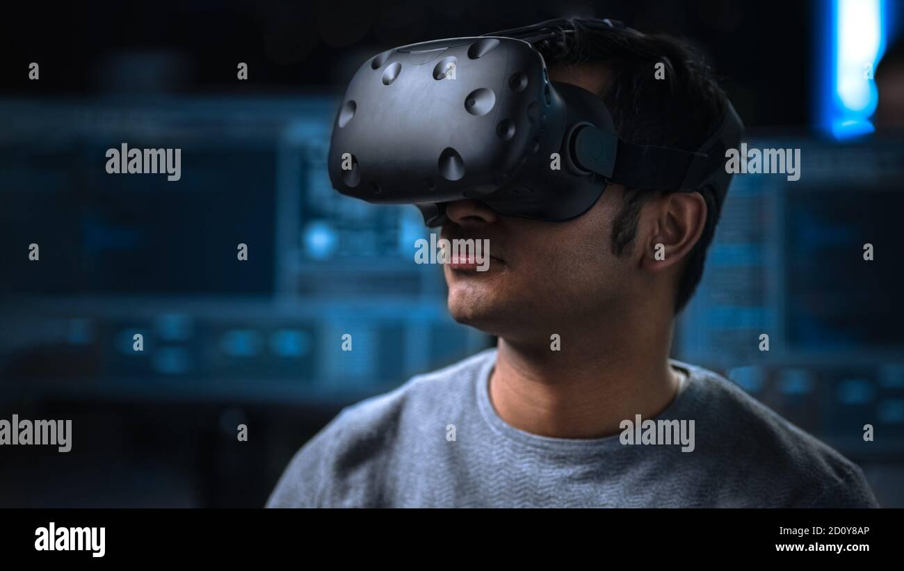 Software Delevoper Wearing Virtual Reality Headset on His Head, Developing and Programming VR Game or Application. In the Background Technology Stock Photo