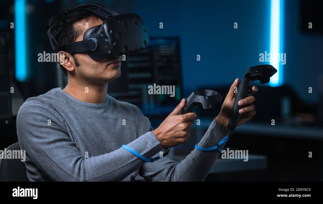Portrait of Software Delevoper Wearing Virtual Reality Headset Using Controllers to Develop and Program VR Gaming and Applications. In Background Stock Photo