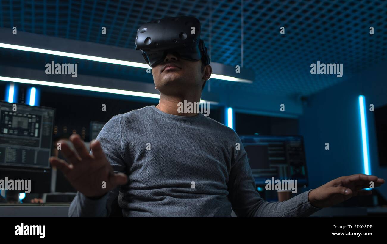 Software Delevoper Wearing Virtual Reality Headset Gesturing with His Head, Developing and Programming VR Game or Application. In Background Stock Photo