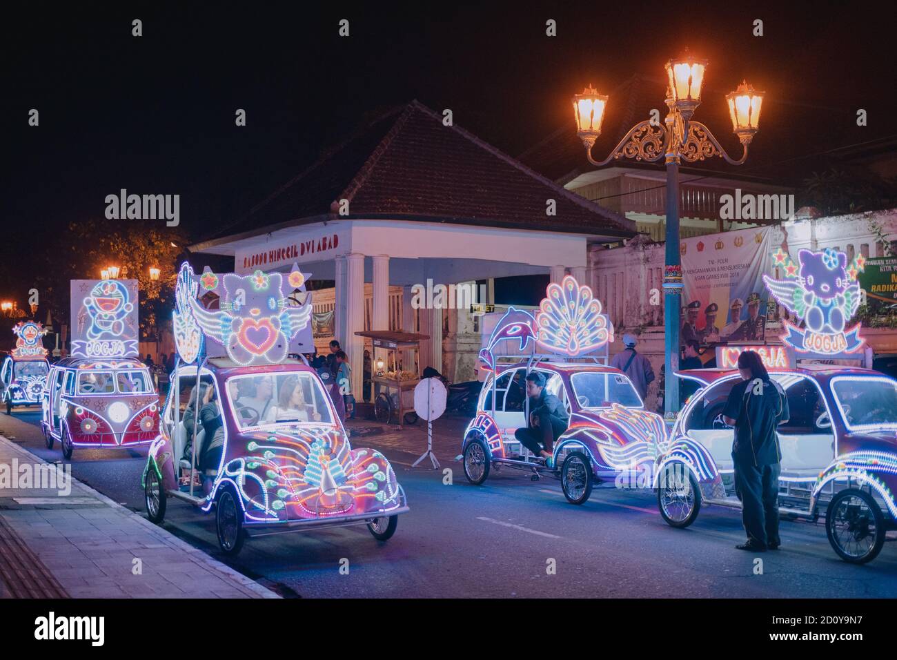 Tourists drive pedicab with colorful lights decoration called Becak Lampu at Alun-alun Kidul Yogyakarta at night Stock Photo