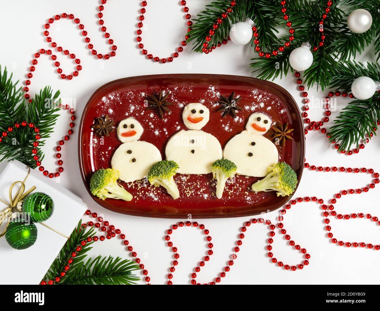 Funny plate with three snowmen made of mozzarella cheese and broccoli. Breakfast idea for kids. Vegetarian food art for New Year or Christmas celebrat Stock Photo