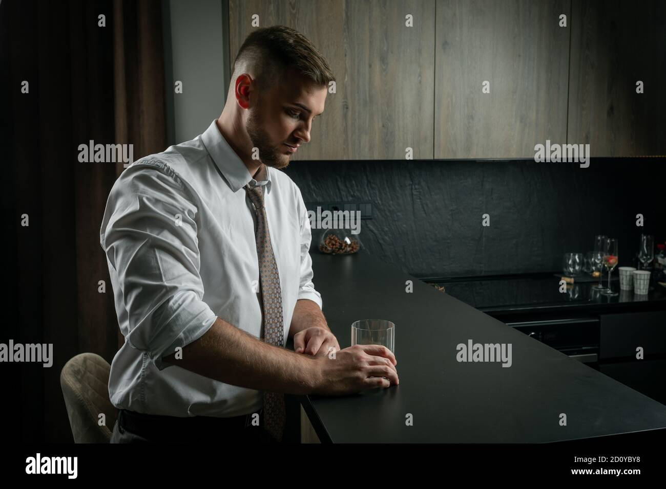 Handsome man wearing suit, drinking whiskey on the kitchen at home Stock Photo