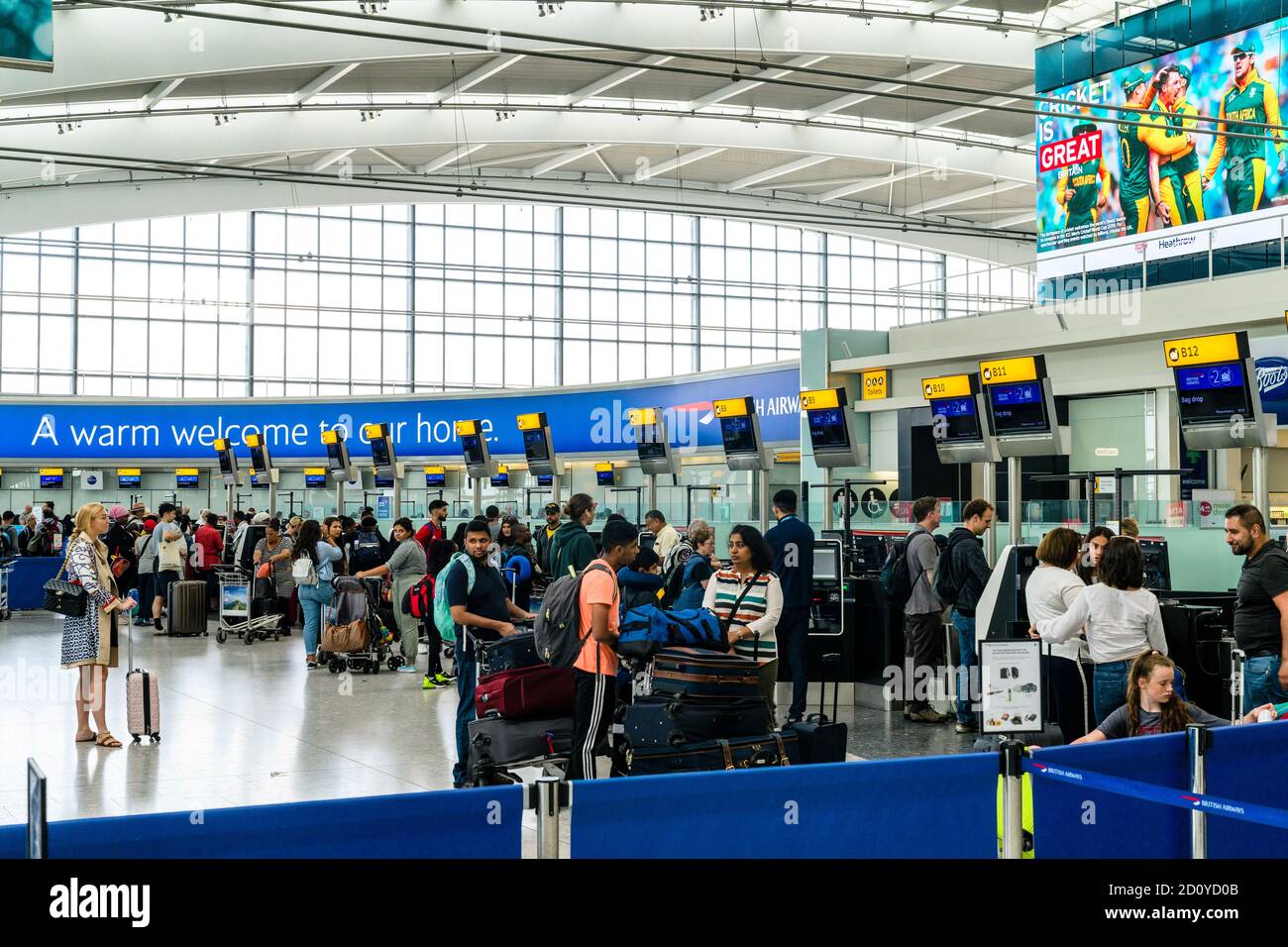 Heathrow airport terminal five, people with trollies of luggage standing in lines waiting to check in at the british Airways counter B1 to B12. Stock Photo