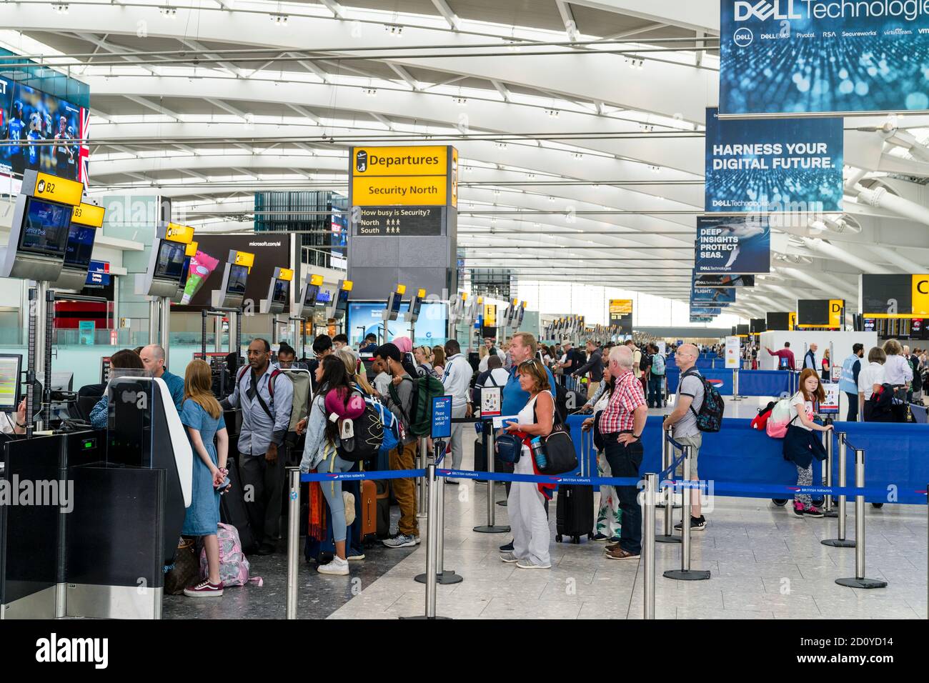 Heathrow airport terminal five, people with trollies of luggage standing in lines waiting to check in at the british Airways counter B1 onwards. Stock Photo