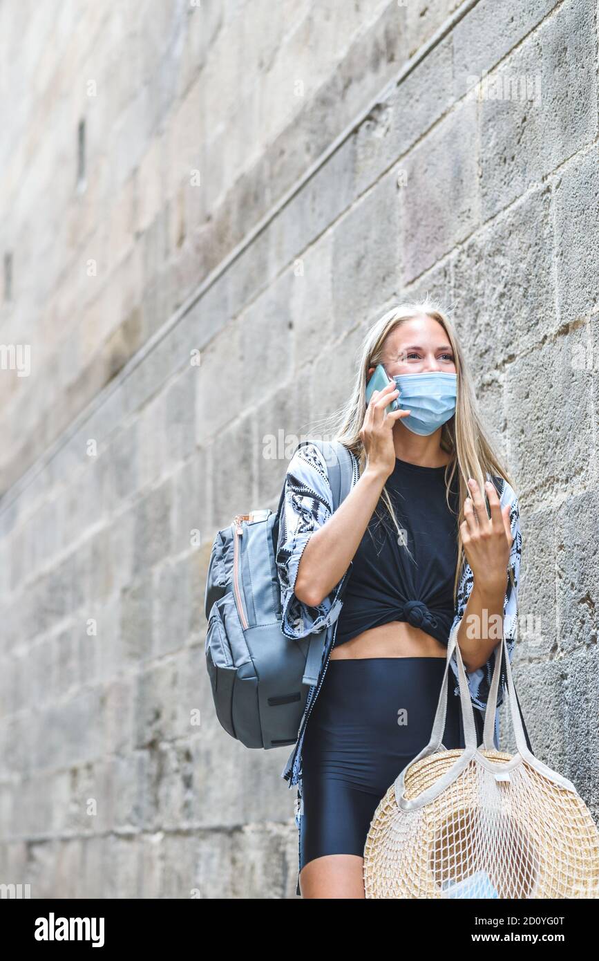 young beautiful caucasian woman wearing a face mask talking by phone in street near a wall with big copy space on the top Stock Photo