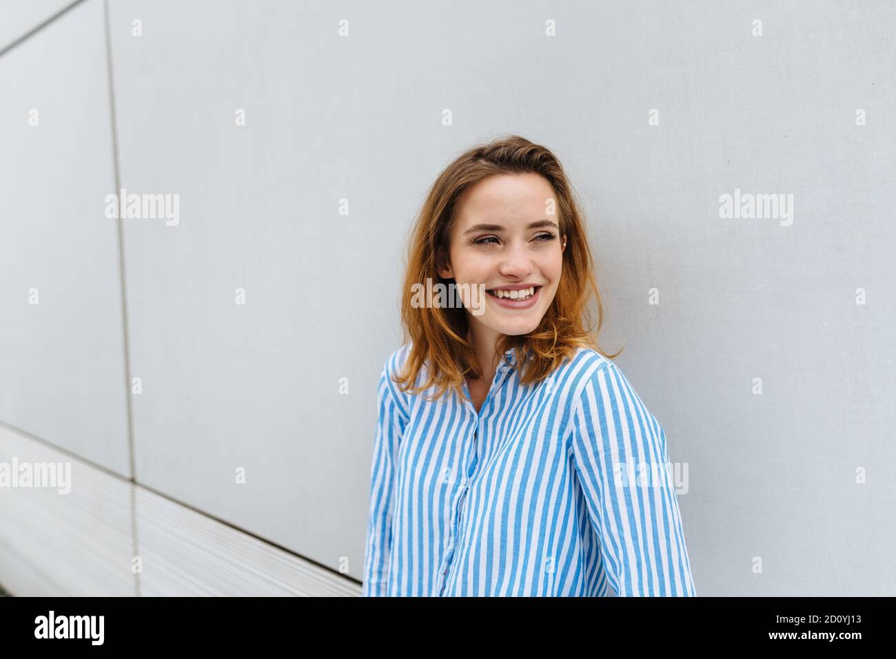 Contented happy young woman smiling to herself as she stands leaning