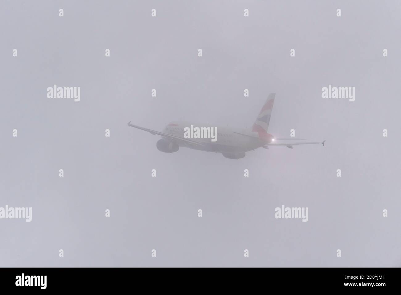 British Airways Airbus A320 jet airliner plane taking off in bad weather from London Heathrow Airport, UK. Disappearing into thick cloud. White out Stock Photo