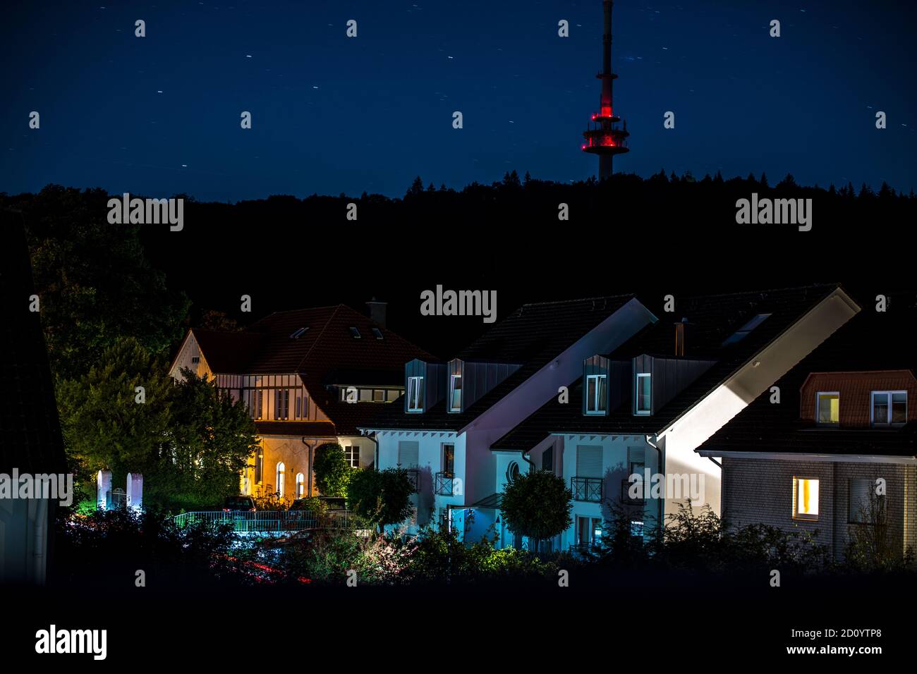 Beleuchtete Häuserreihe eines Wohngebiets bei Nacht, im Hintergrund der Waldhang mit Fernsehturm Stock Photo