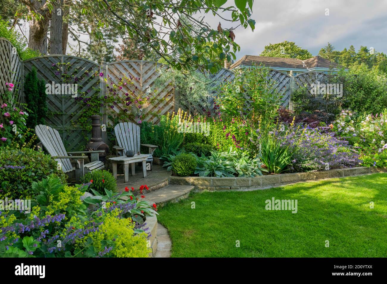 Landscaped sunny private garden (contemporary design, colourful summer flowers, border plants, patio furniture seating, lawn) - Yorkshire, England, UK Stock Photo