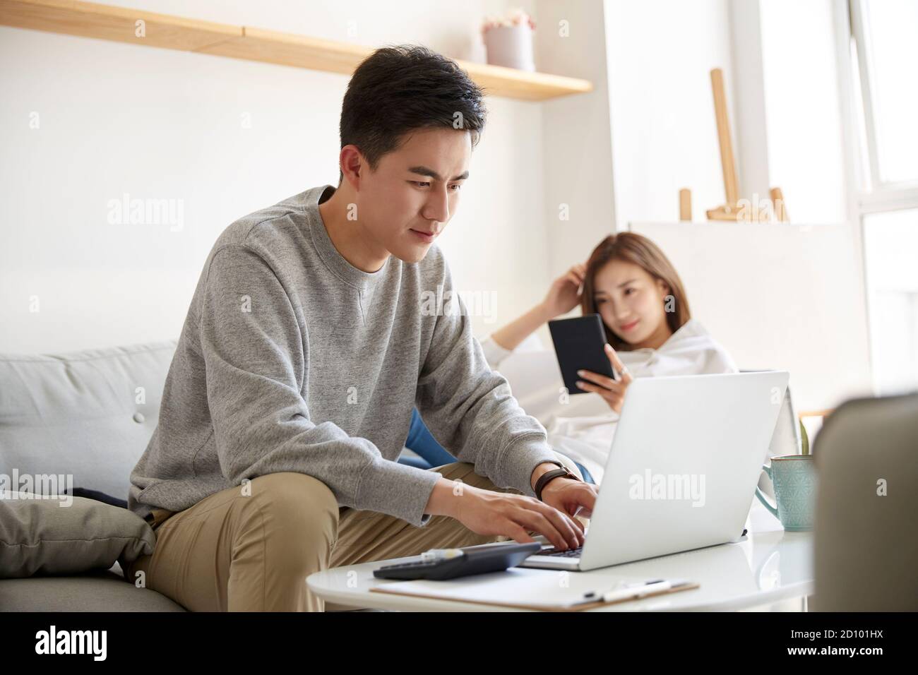 young asian couple staying at home with husband working using laptop