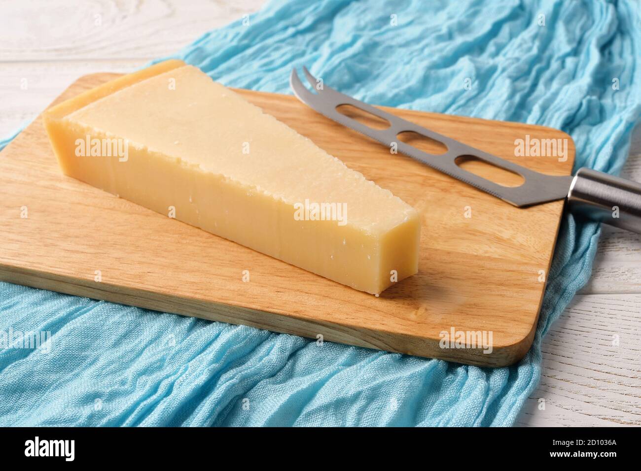 triangular wedge of traditional italian hard cheese grana padano or parmesan and cheese knife on a wood cutting boad over white wood table front view 2D1036A