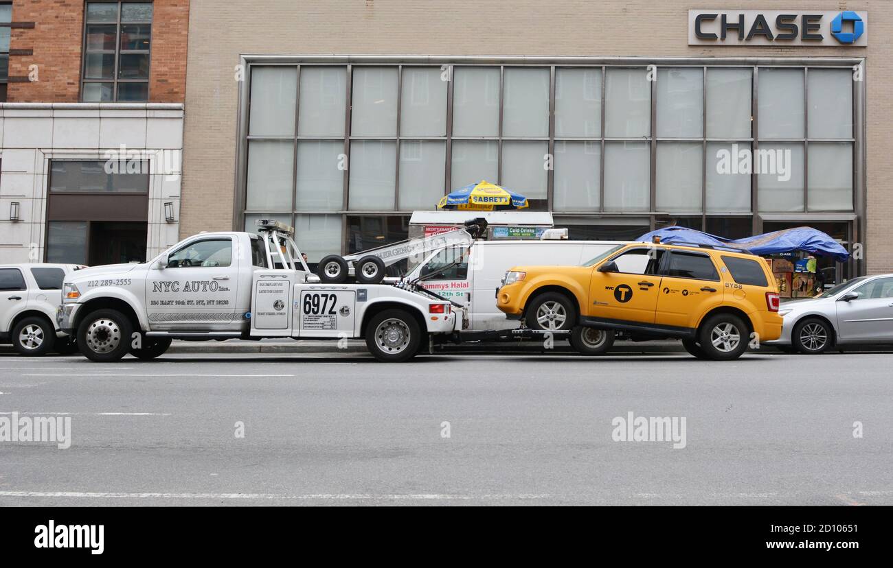 NEW YORK, USA - MAY 10, 2019: Broken down yellow taxi cab being towed away by a recovery vehicle, outside a Chase bank branch in New York City on May Stock Photo