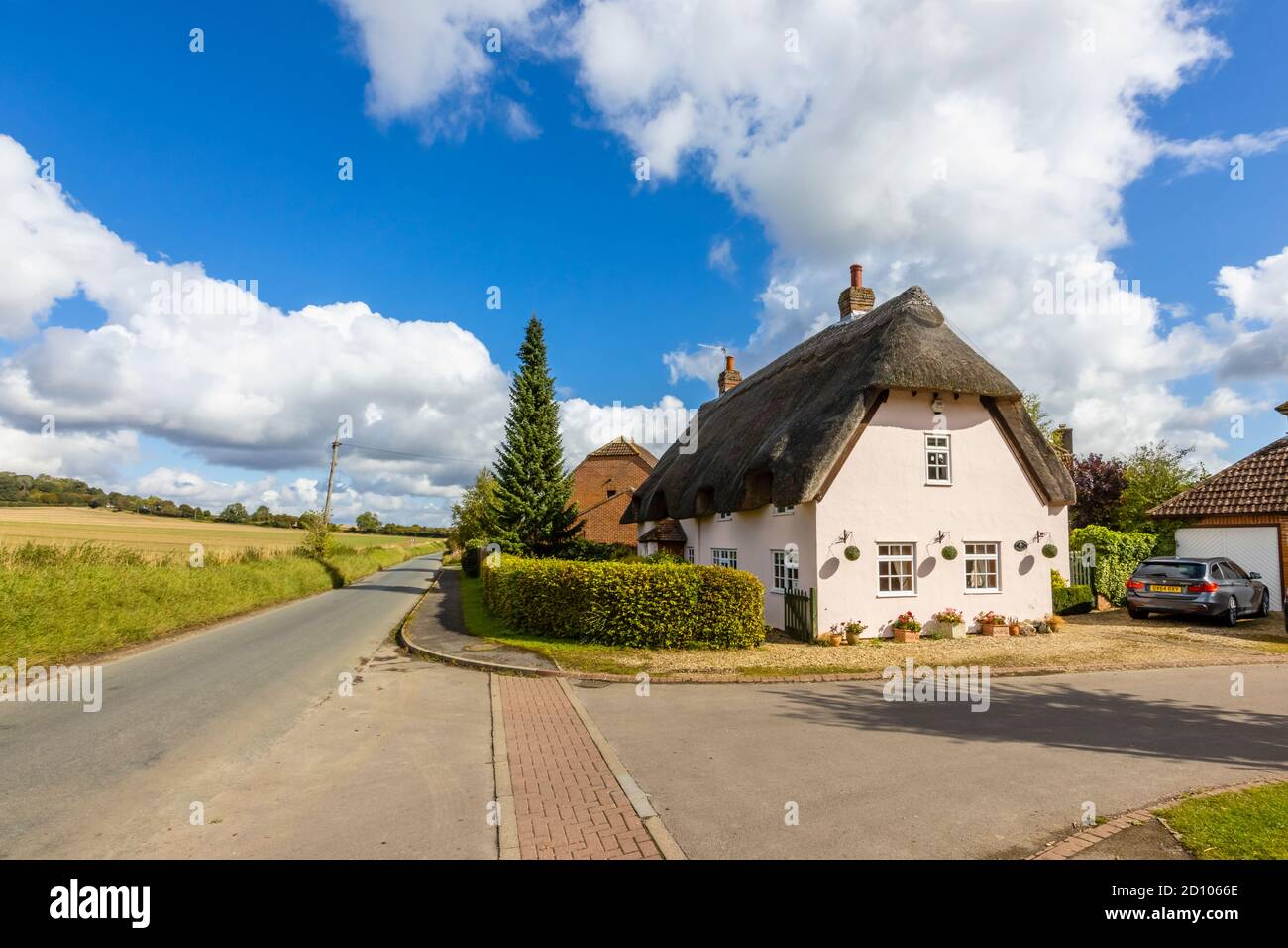 A thatched pink cottage on a rural country lane by open fields in Great Bedwyn, a village in east Wiltshire, southern England Stock Photo
