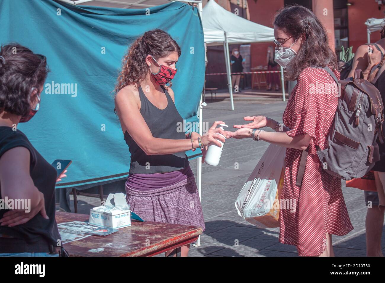 Bologna: young volunteer sanitizes the hands of a customer before entering the outdoor fruit and vegetable market (Covid-19 2020 pandemic) Stock Photo