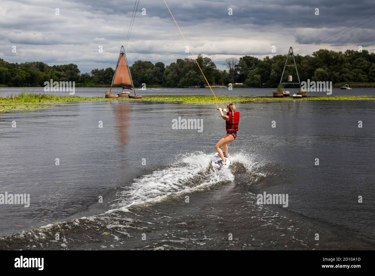 Young pretty slim brunette woman riding wakeboard on in a summer lake. Wakeboarding on cable Stock Photo