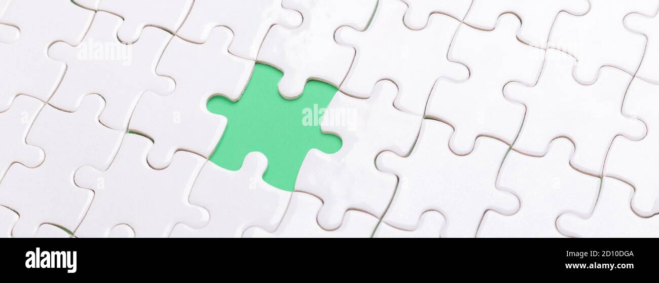 White jigsaw puzzle with with one piece missing and green background - Image Stock Photo