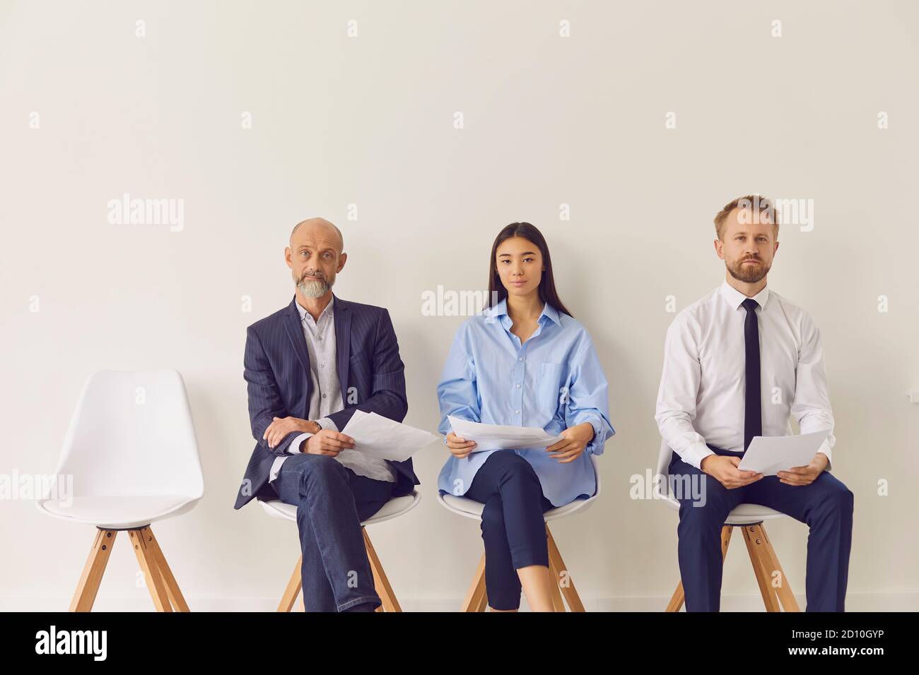 Three multiracial candidates of different ages sitting on chairs waiting for job interview Stock Photo
