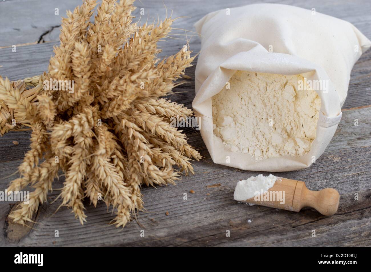 Flour sack, ears and wooden measuring cup on wooden background. Natural baking products. Stock Photo