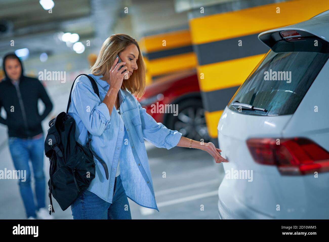 Criminal man in black hoodie approaching young woman opening car on parking Stock Photo