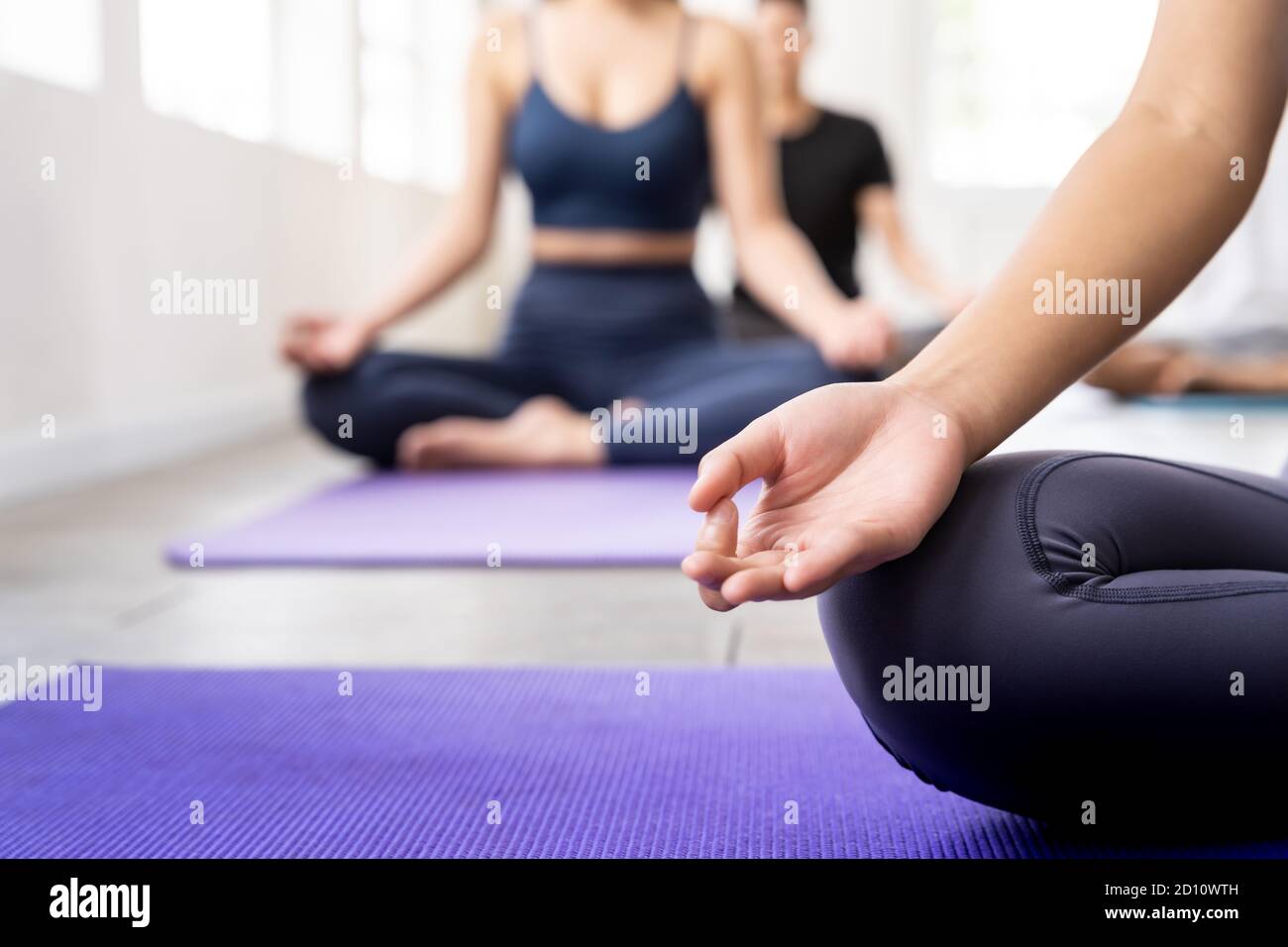 Close up of sporty attractive asian coach on Lotus pose position sitting Padmasana with background of student practicing yoga lesson. Work out fitness Stock Photo