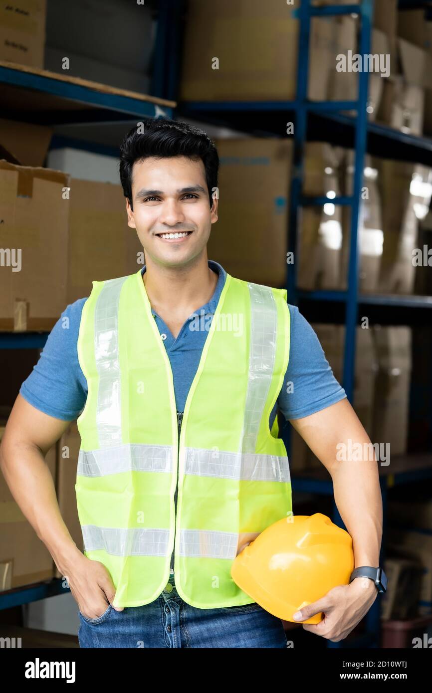 Portrait of Indian asian warehouse worker with safety vest stand and hold yellow helmet in