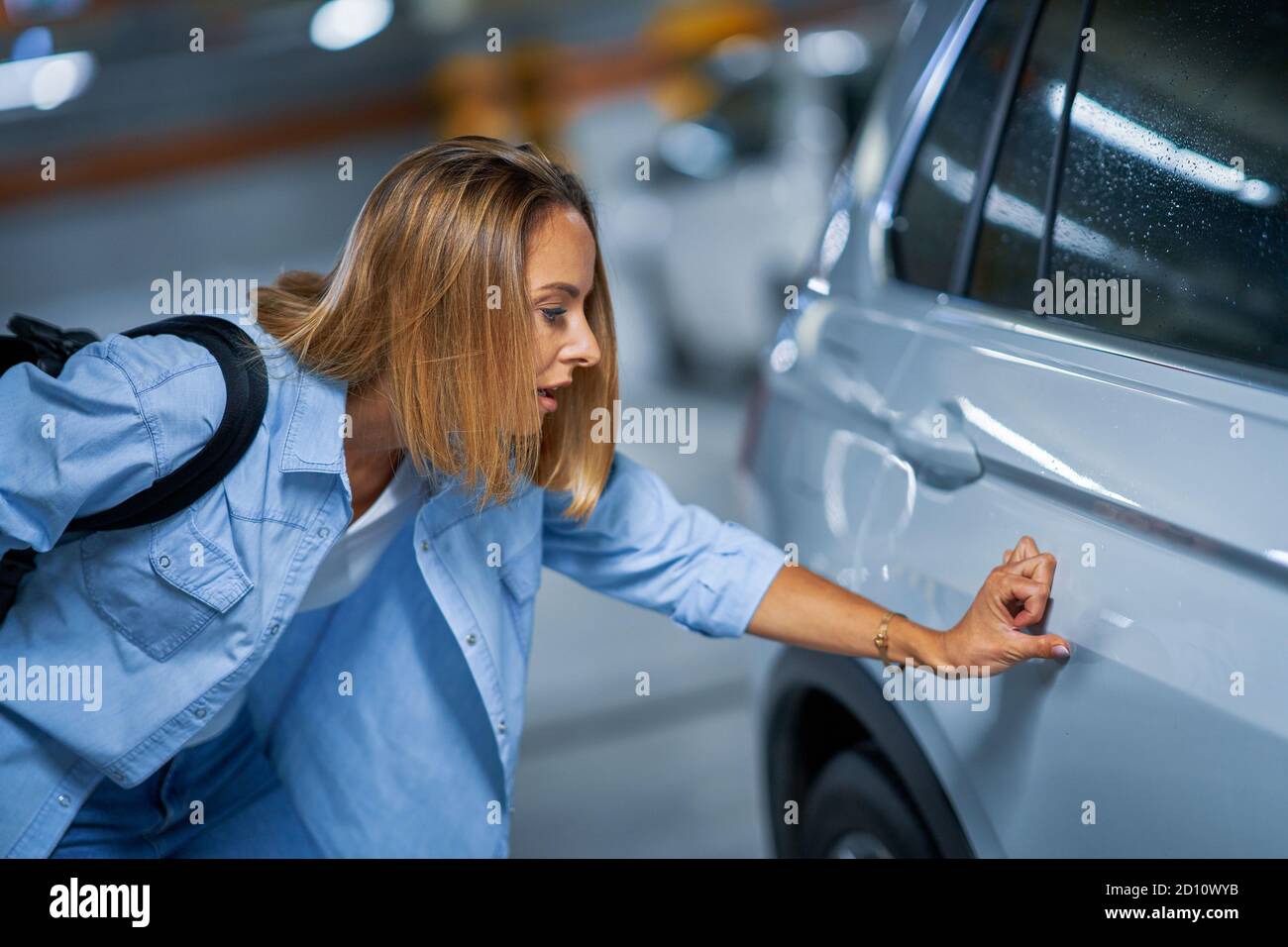 Portrait of young woman with scratched car at underground parking lot Stock Photo