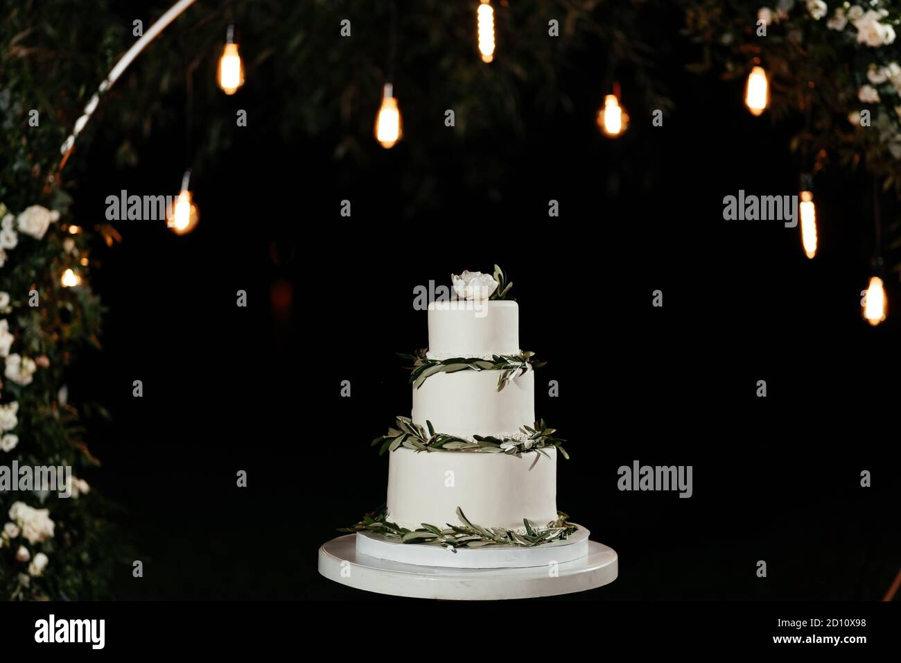 Three-tier minimalistic wedding cake at the background of the lights. Cake at the wedding Stock Photo