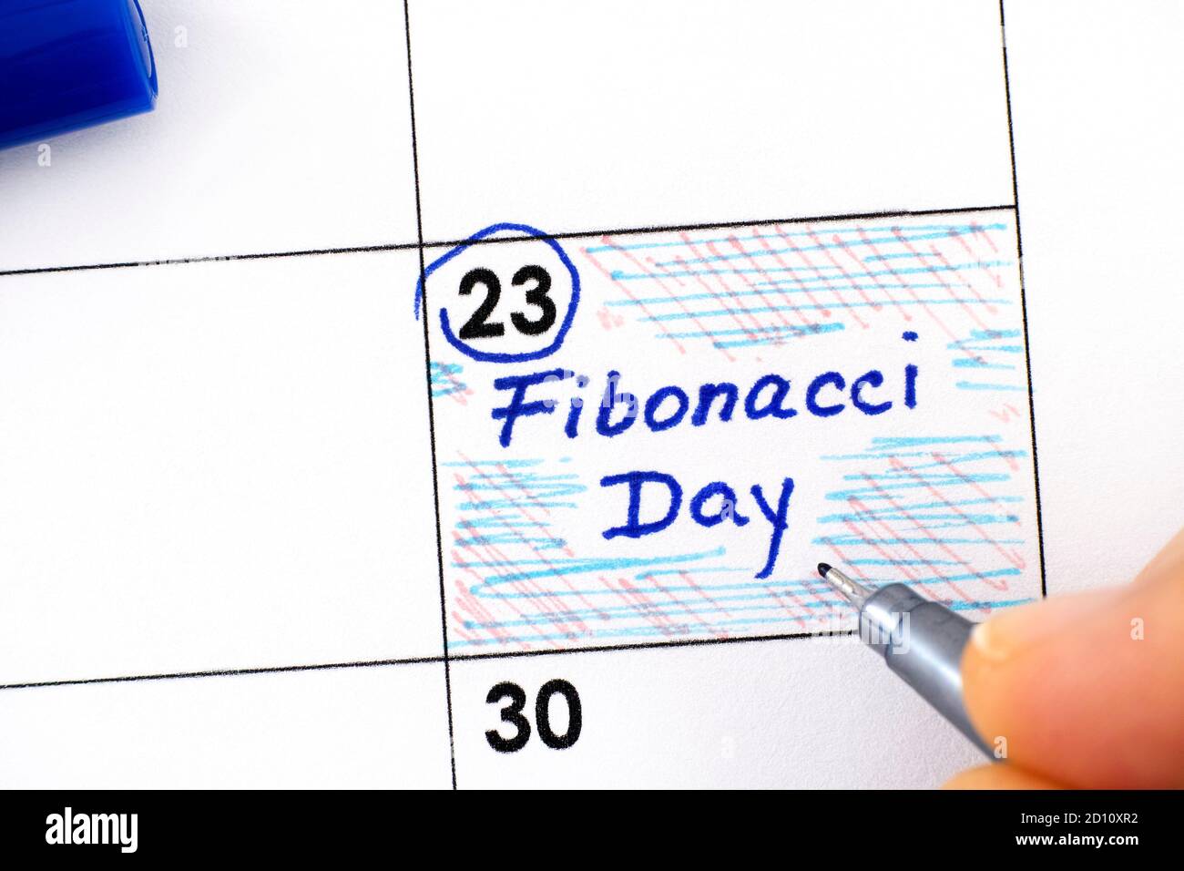 Woman fingers with pen writing reminder Fibonacci Day in calendar. November 23. Stock Photo