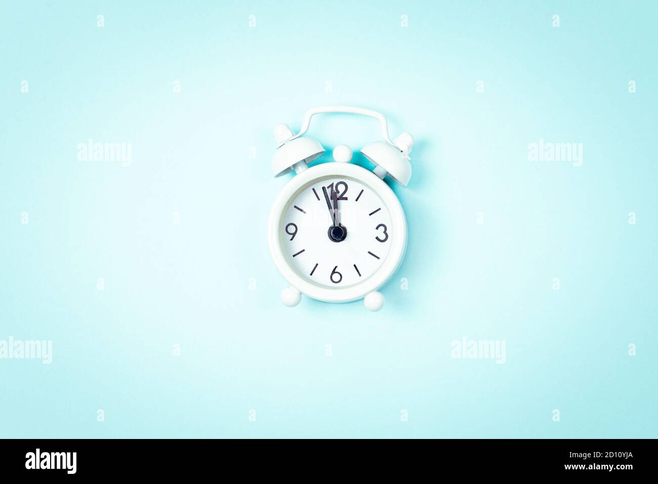 White vintage style alarm clock showing five minutes left untill midnight over blue background. New Year advent. Stock Photo