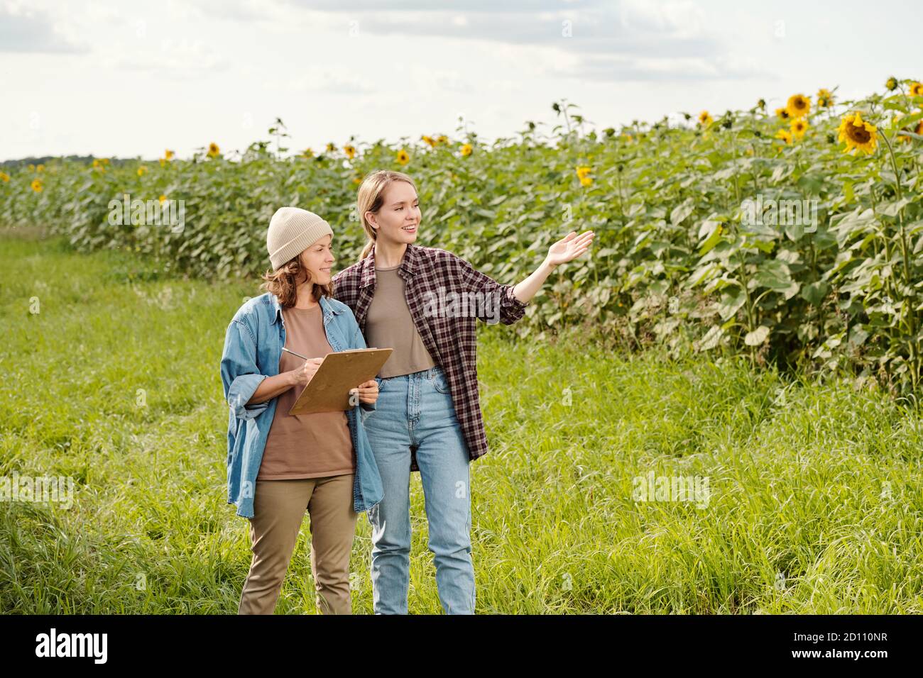 Two cheerful farmers in workwear looking at sunflower field in front of camera Stock Photo