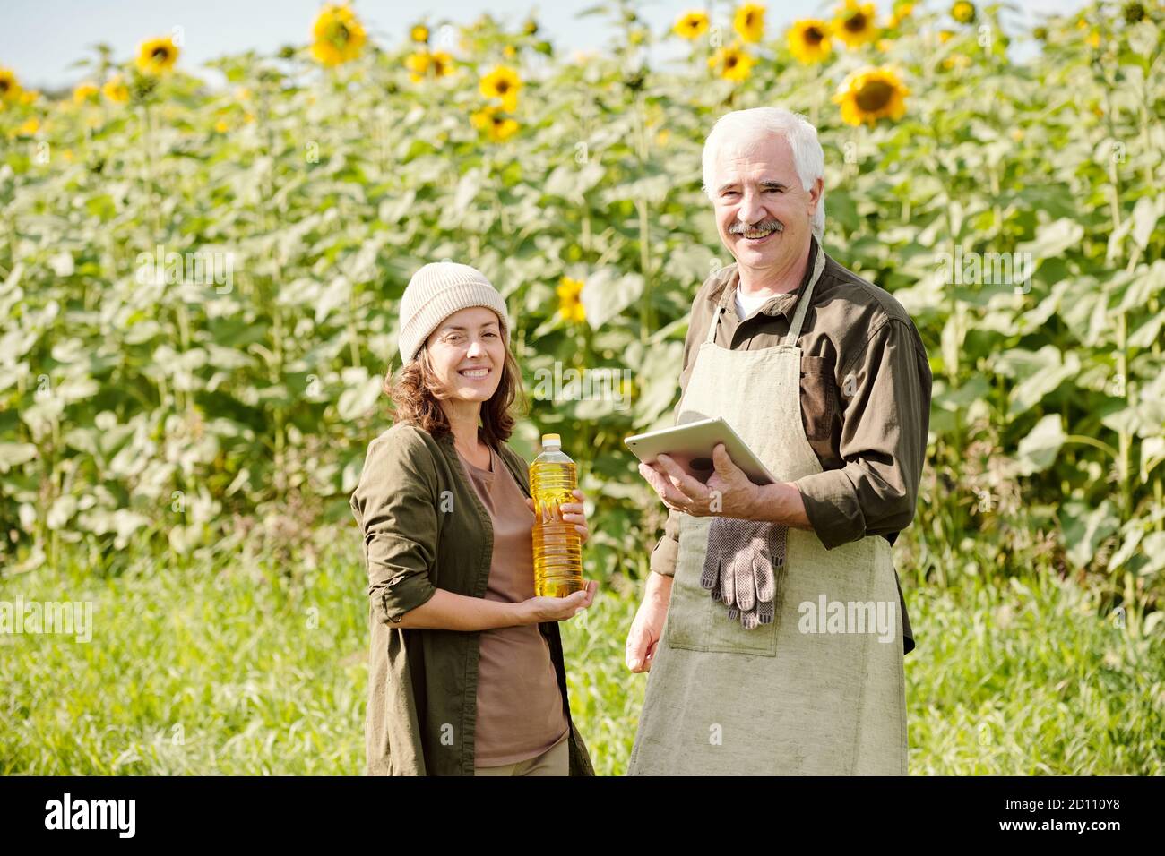Happy senior male farmer and his mature female colleague with bottle of oil Stock Photo