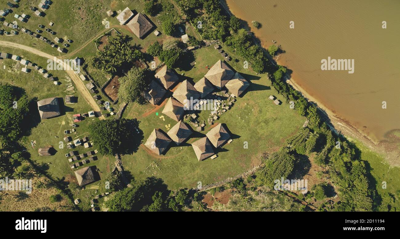 Top down traditional village at green grass valley on sea coast aerial view. Indonesia landscape of tropical nature at sand ocean bay. Unique buildings at countryside road in birds-eye drone shot Stock Photo