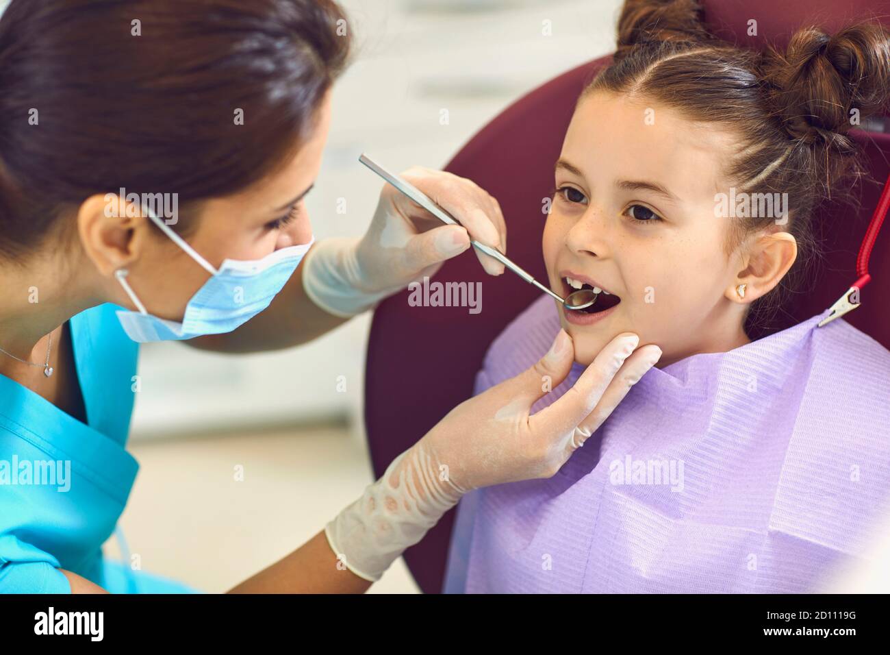 Woman dentist examining smiling child girls teeth with mirror in dental