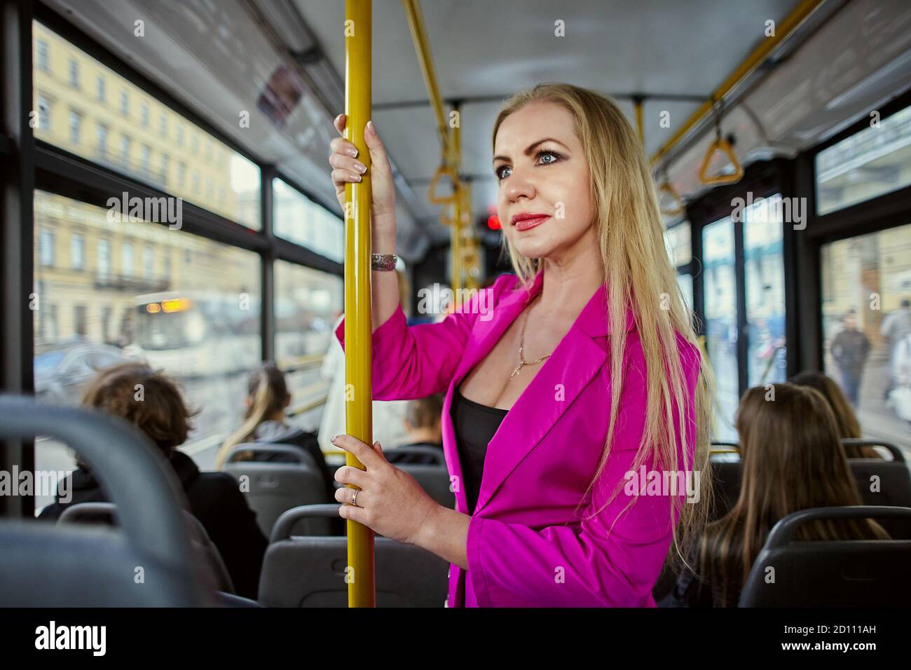 Caucasian woman dressed in pink, stands inside a bus or trolleybus. White female rides while standing in the passenger cabin of public transport and h Stock Photo