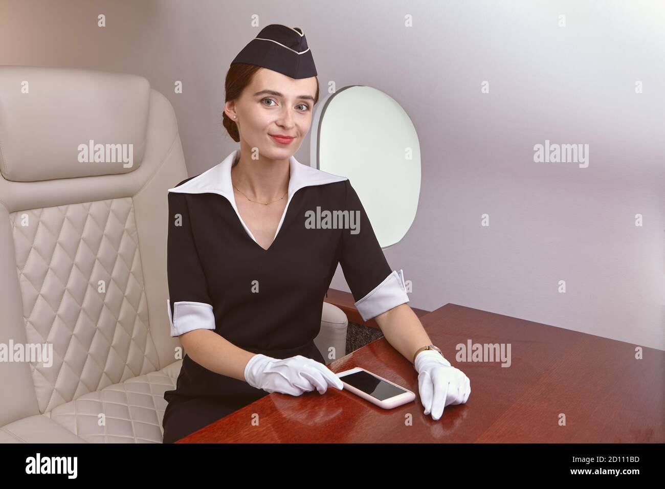 Air steward in passenger cabin inside plane. The flight attendant sits in an airplane seat near the window. Stock Photo
