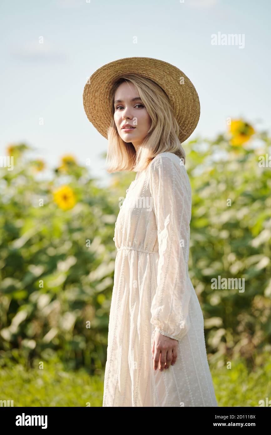 Gorgeous young blond woman in straw hat and white dress standing outdoors Stock Photo