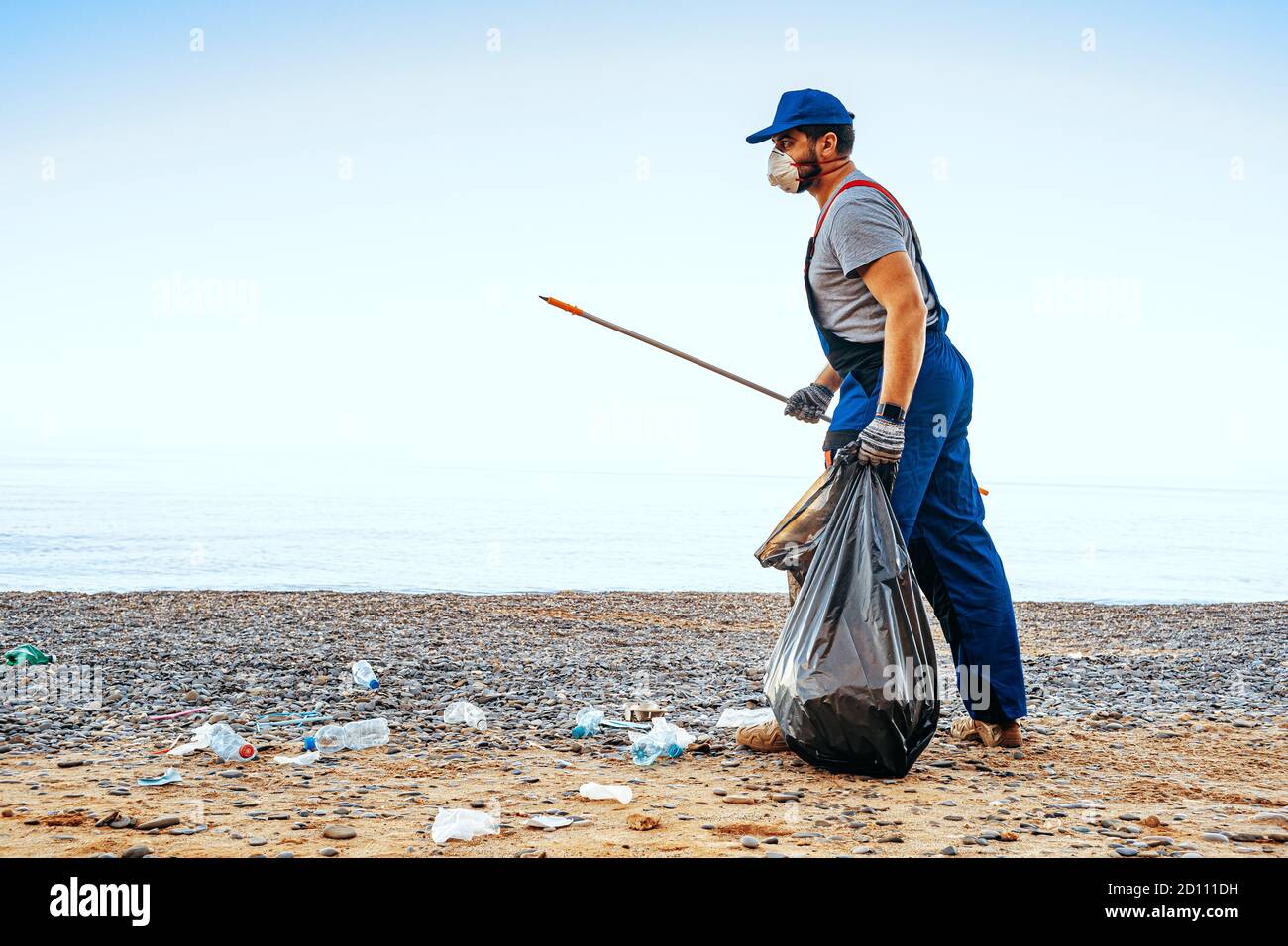 Man volunteer collecting garbage on the beach with a reach extender ...