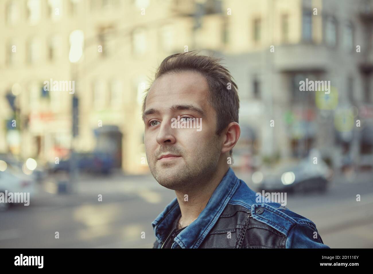 The face of a serious Russian man against the background of a city street on a summer evening. Close up portrait of Caucasian male outdoors. Stock Photo
