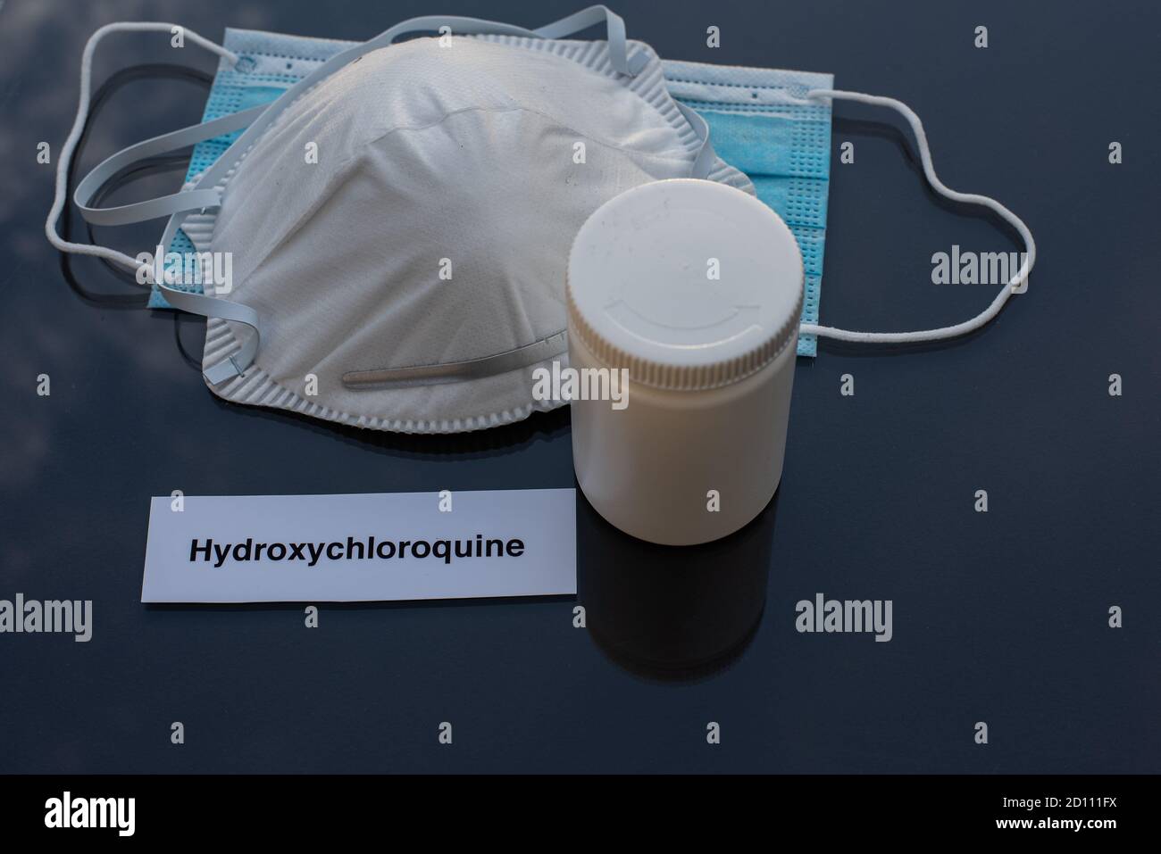 hydroxychloroquine in a gallipot for treatment of covid-19 and two masks as protection on black reflective table top, Denmark, October 4, 2020 Stock Photo
