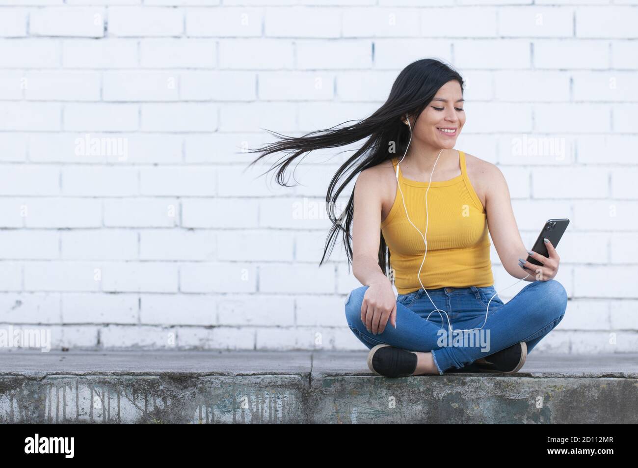 Young Latin woman listening to music with headphones and smiling near ...