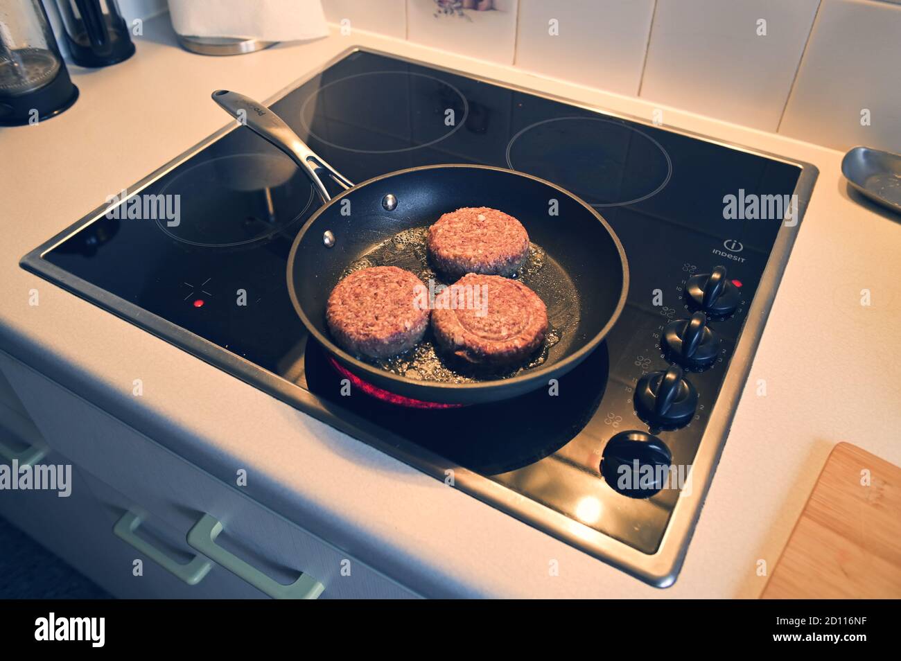 Side angle of three beefburgers cooking in a frying pan on a hob oven