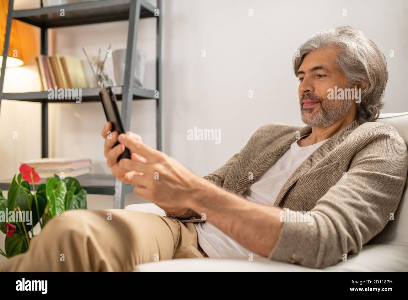 Mature bearded man in casualwear sitting in comfortable armchair at home Stock Photo