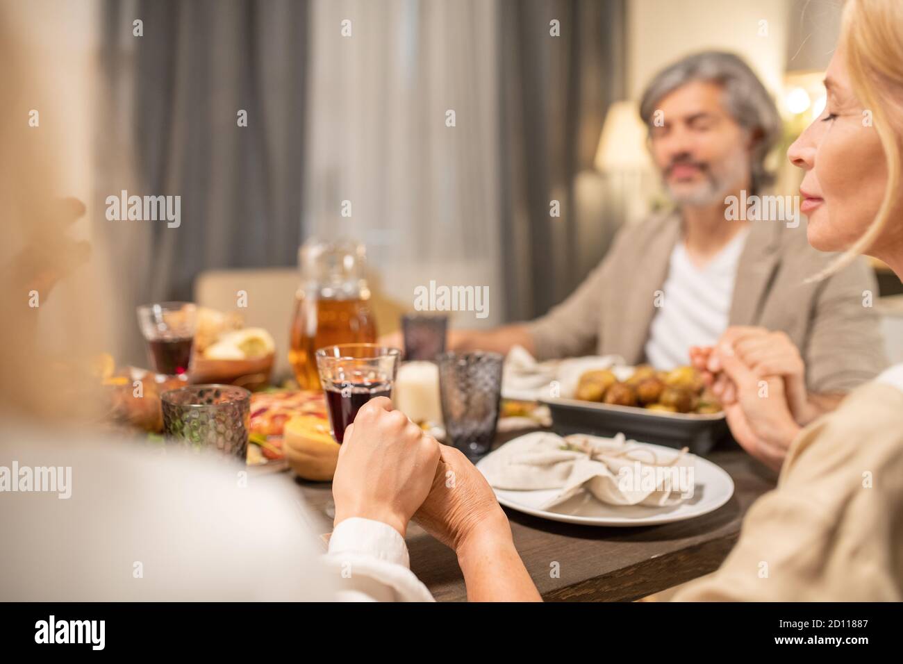 Hands of family members saying thanks to Lord in Thanksgiving prayer by table Stock Photo