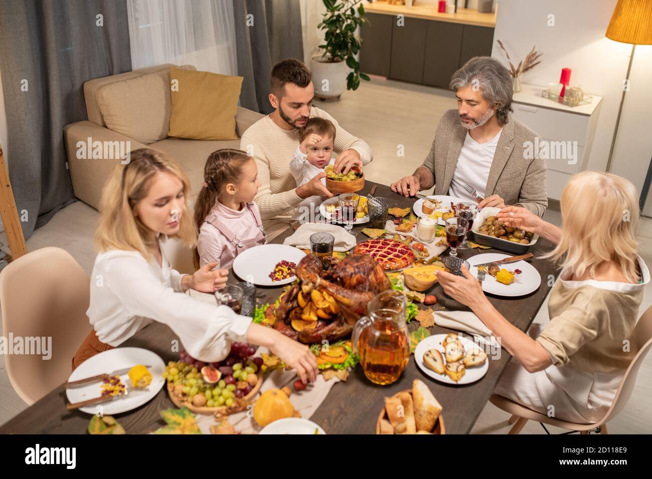 Young father giving fresh fruits to his little son by large served festive table Stock Photo