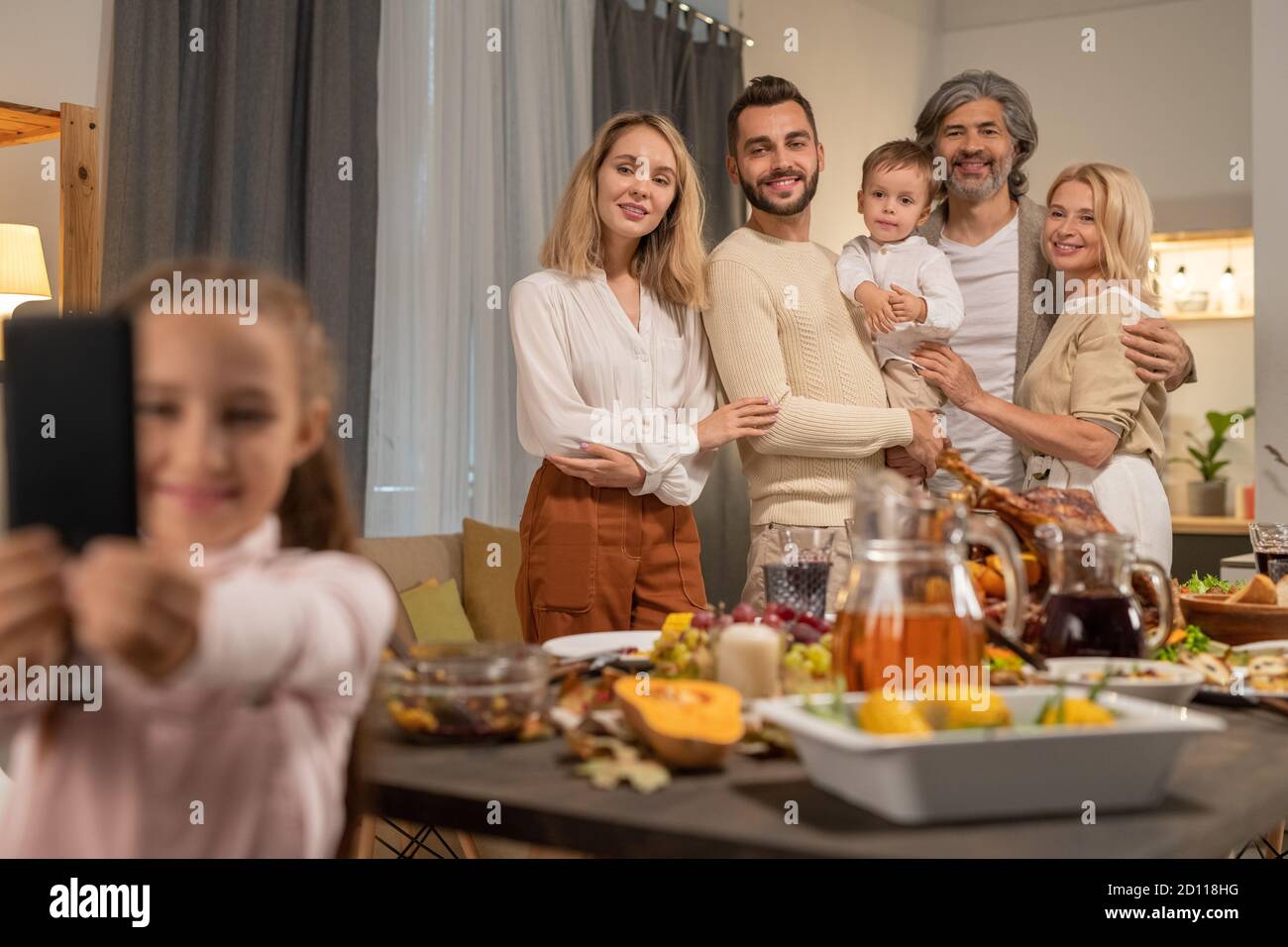Joyful large family standing by festive table and looking at smartphone camera Stock Photo